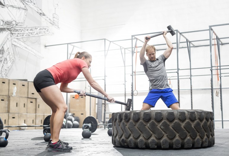 Man and woman hitting tire with sledgehammer in crossfit gym